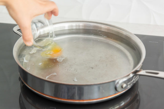 Pouring Egg from Glass Bowl into Hot Water in Saucepan