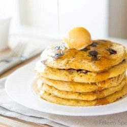 Cornmeal Pancakes Stacked on a Plate with Butter and Maple Syrup Pouring On Top
