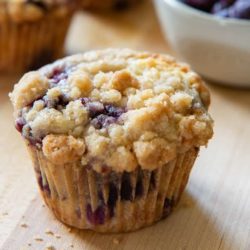 A close up of a blueberry muffin with jammy purple blueberry spots and golden crumbs on top