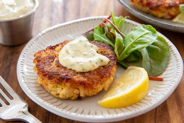 Panko Crab Cake Recipe - served on a White Plate with Lemon, Tartar Sauce, and Greens