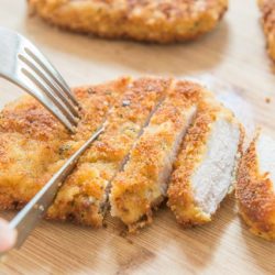 Parmesan Crusted Pork Chops Served On a Wooden Platter with a Fork and Knife Slicing Into Pieces