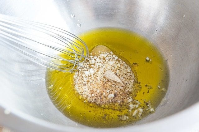Olive Oil, Vinegar, Mustard, Garlic, and Seasoning in Mixing Bowl with Whisk