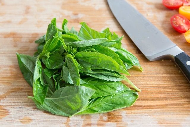 Fresh basil leaves on wooden board with knife