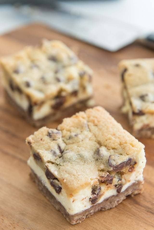 Squares of Cheesecake Bars with Chocolate Chip Cookie Dough Top on Wooden Board
