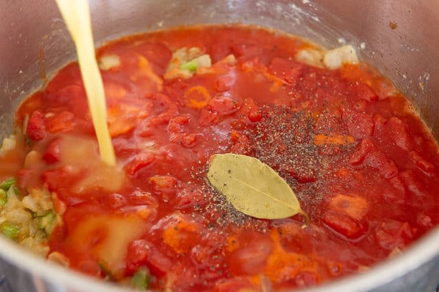 Pouring Chicken Stock Into Pot with Tomatoes, Bay Leaf, and Pepper