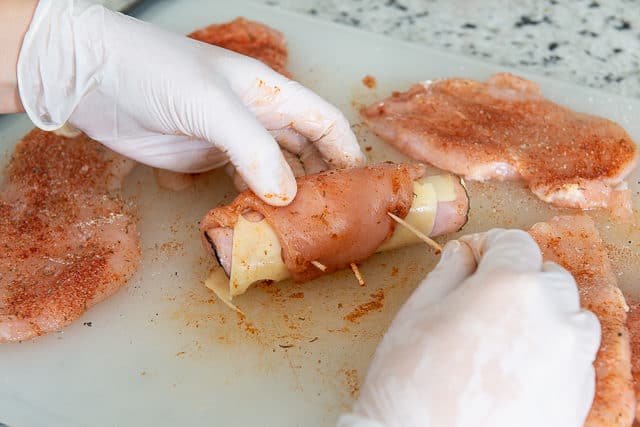 Rolling chicken with ham and cheese and securing with toothpicks