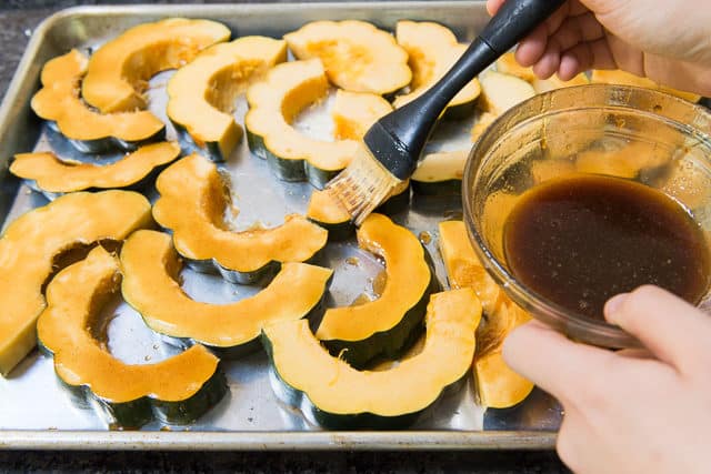 Acorn Squash Slices on a Sheet Pan Being Brushed with maple Butter