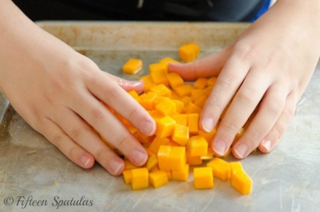 tossing butternut squash cubes with maple, oil, salt and pepper