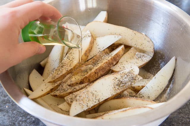 Pouring Oil and Seasoning Onto Russet Potato Wedges in Bowl