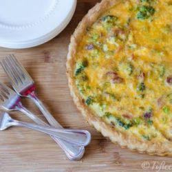 Whole Broccoli Cheddar Quiche on Cutting Board with Forks and Plates