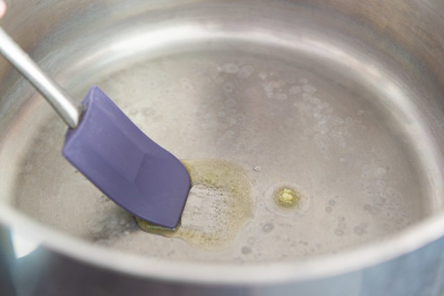 Spreading ghee in pot with purple spatula