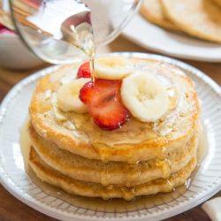 Whole Wheat Pancakes Stacked On a Plate with Maple Syrup Pouring Over The Top