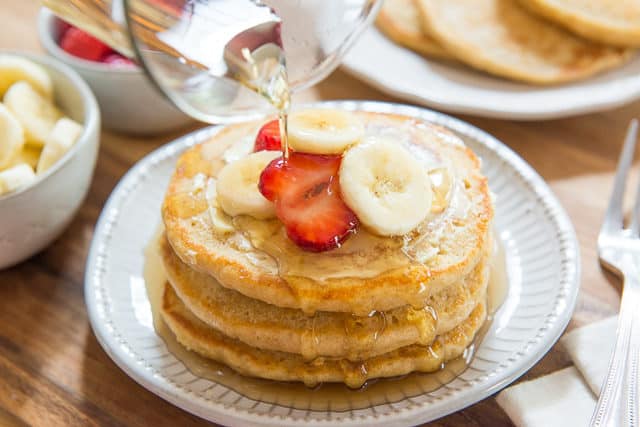 Whole Wheat Buttermilk Pancakes - Stacked on a Plate with Strawberries, Bananas, and maple Syrup on Top