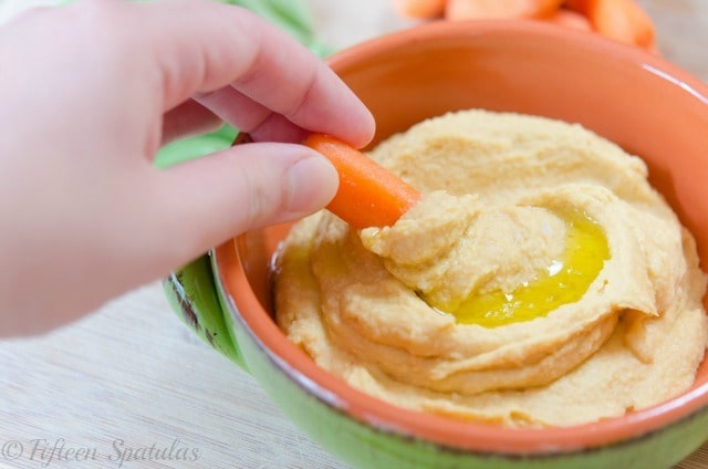 A close up of a bowl of hummus with carrot stick