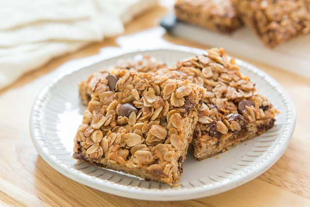 Chocolate Chip Granola Bar Squares on a White Plate on Wooden Board