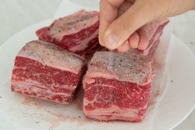 Sprinkling Four Raw Beef Short Ribs with Salt and Pepper