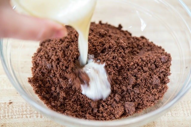Pouring Butter Into Crushed Chocolate Wafer Crumbs in Bowl