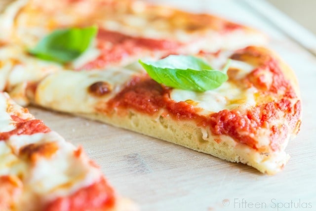 A close up of a slice of pizza made with basil and cheese