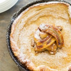 Caramelized Banana Topped Dutch Baby in Cast Iron Sprinkled with Confectioner's Sugar