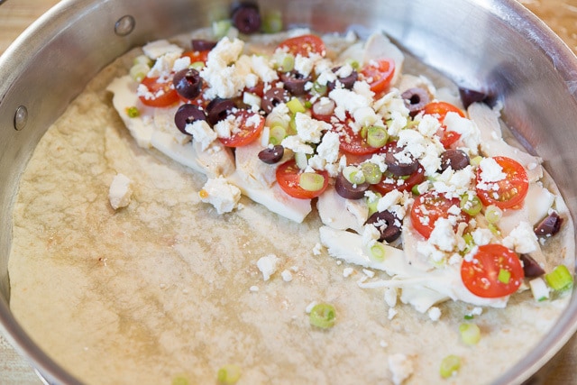 Flour Tortilla in Skillet with kalamata olives, feta, tomatoes, and chicken on one half