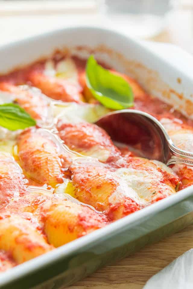 Stuffed Shells - In Green Casserole Dish with Basil Leaves and Spoon