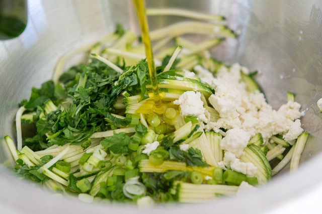 Adding Olive Oil to a Bowl with Shredded Zucchini, Scallions, Herbs, and Feta