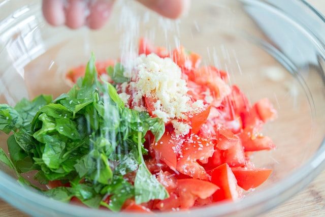 Sprinkling Salt on Basil, Garlic, and Tomatoes in Bowl