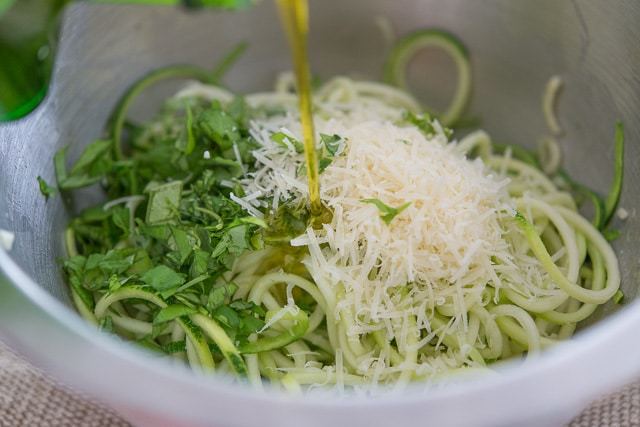 Pouring Olive Oil Into Zoodle Mixing Bowl with Cheese and Herbs