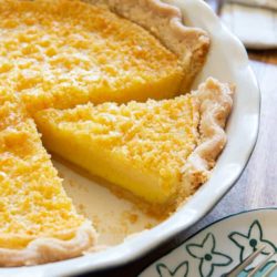 A slice of lemon buttermilk pie in blue pie dish separated from full pie