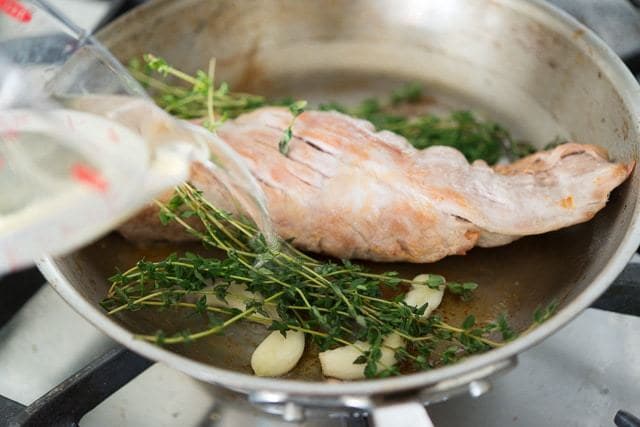 Pouring Chicken Stock Into Pan to Deglaze with Herbs and Garlic