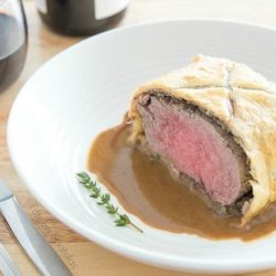 Beef Wellington Sliced and Plated in White Bowl with Pan Sauce