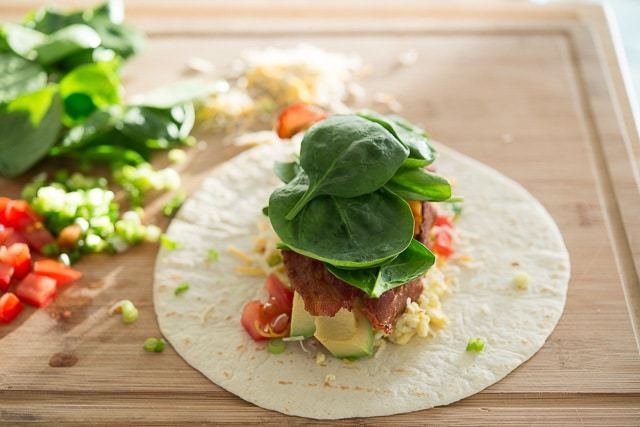 Spinach Leaves Added On Top of Burrito Ingredients on Tortilla
