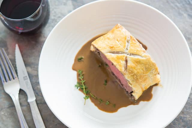 Beef Wellington Recipe - Plated Over Pan Sauce with Thyme Sprigs in White Bowl