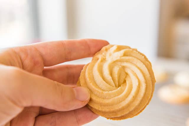A Danish Butter Cookie Held Up by Hand to Show Swirl Shape