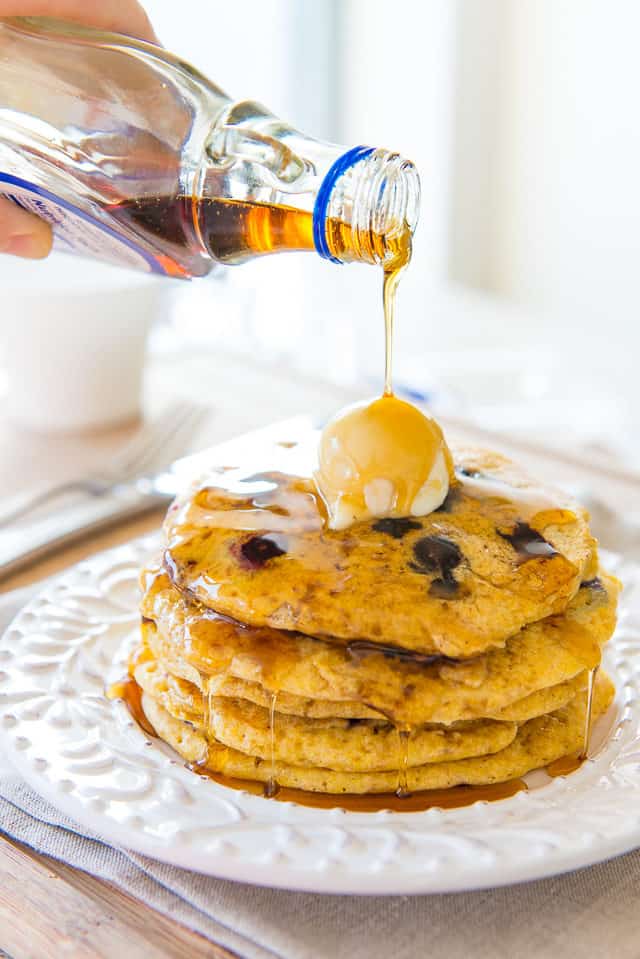 Cornmeal Pancakes - Stacked on a Plate with Butter and Maple Syrup Pouring On Top