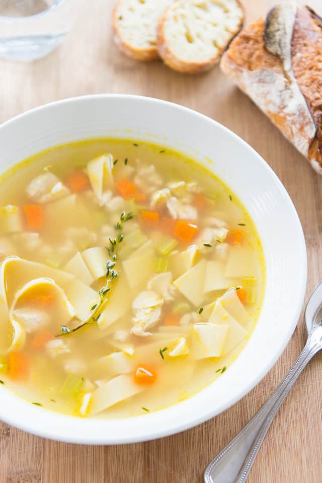 Chicken Noodle Soup Recipe - Served in a White Bowl with Bread on Wooden Board