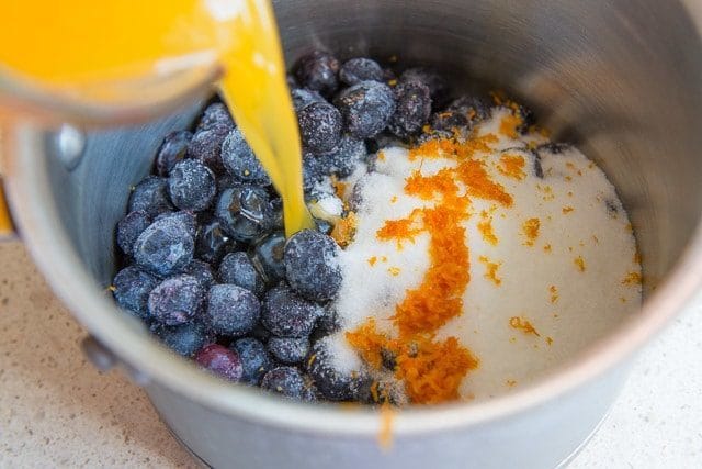 Pouring Orange Juice Into Pan with Blueberries, Sugar, and Orange Zest