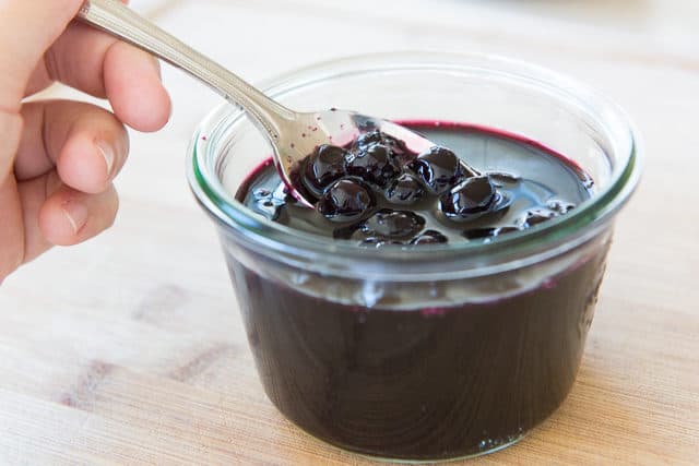 Blueberry Sauce Recipe - Shown in Glass Jar with Spoon Full of Softened Blueberries