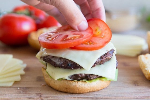 Adding Fresh Tomato Slices to Bun with Two Beef Patties and Cheese Slices