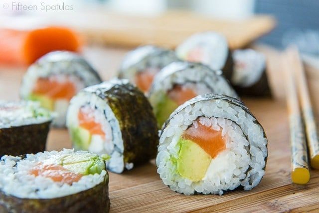 Sushi Recipe - Sliced to See Filling Of Avocado, Salmon, and Cream Cheese on Wooden Board