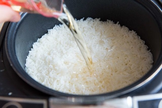 Cooked Sushi Rice in Cooker with Vinegar Being Poured In