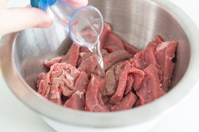 Beef Sirloin Strips Raw in Mixing Bowl with Liquid Seasoning Added