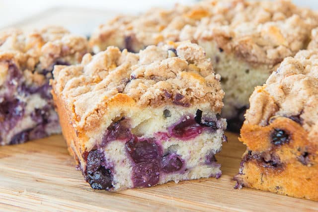A close up of a piece of blueberry buckle cake on a wooden board