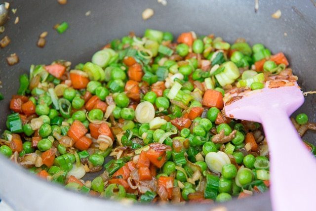 Softened vegetables in pan including peas, carrots, scallions