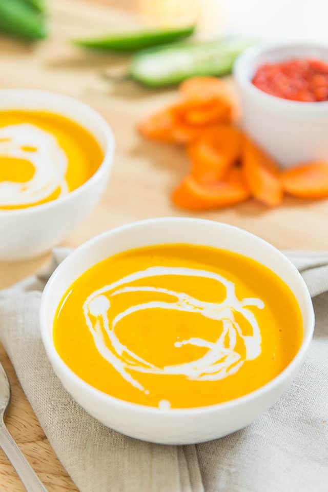 Two Bowls Of Carrot Coconut Soup with Jalapeno and Harissa On Linen Napkin With Coconut Milk Swirl Decoration