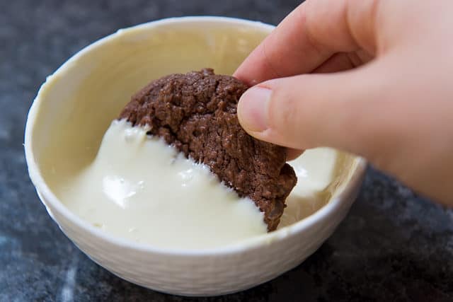 Dipping Chocolate Cookie Into Melted White Chocolate In Basket Ceramic Weave Bowl