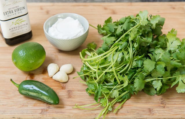 Fresh cilantro, garlic cloves, jalapeno, lime, yogurt, and olive oil on wooden board for creamy cilantro dressing