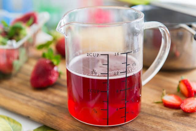 Strawberry Syrup for Drinks - in Measuring Cup on Wooden Board