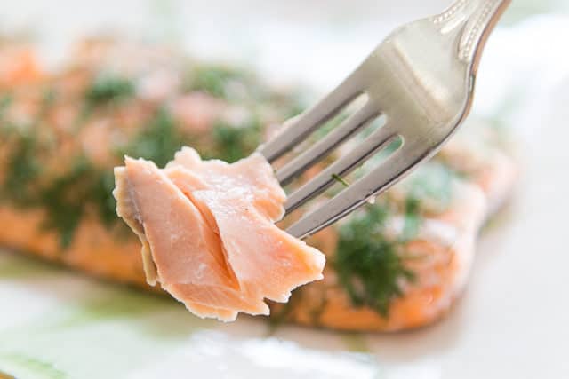 A close up of a plate of food with a fork showing moist salmon baked in oven