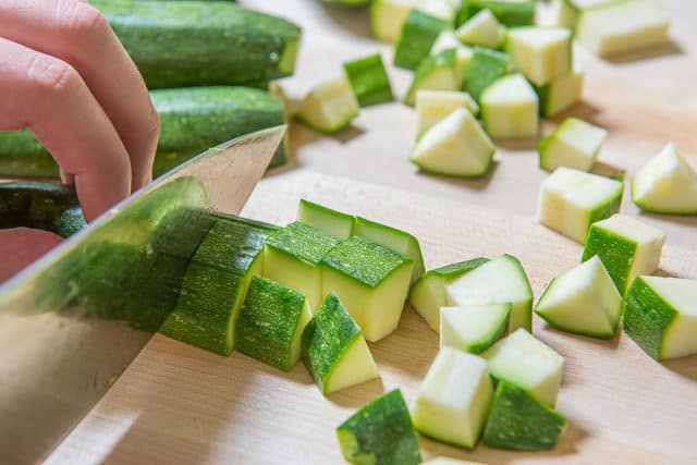Knife Cutting Fresh Zucchini on Board Into Bite Size Pieces